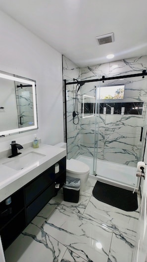 Ein modernes Badezimmer mit einer Duschkabine aus Glas, einem weißen Waschbecken und einem Boden mit Marmorfliesen.