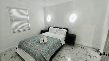Quarto com cama, mesa de cabeceira, janela com persianas e porta.