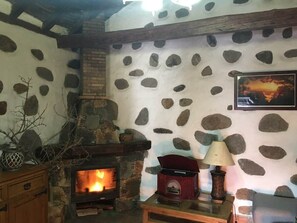 Un intérieur rustique avec un mur en pierre, une cheminée, une table en bois et une lampe.