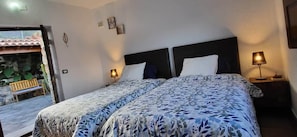 Ein Schlafzimmer mit zwei Betten, einer Bank vor der Tür und Blick auf einen Garten.