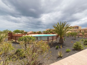 A swimming pool surrounded by a wooden fence, with desert plants and a cloudy sky. - VvCasa Maruca (Internet Access - 1 GB) (Castillo Caleta de Fuste)