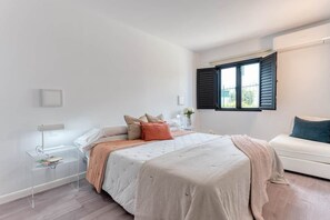 Un dormitorio con cama, mesita de noche, lámpara y una ventana con persianas.