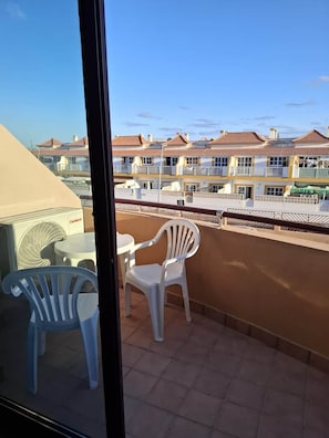 Ein Balkon mit zwei weißen Plastikstühlen und einem Tisch, mit Blick auf eine Reihe von Gebäuden mit roten Ziegeldächern.