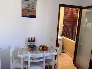 Ein Essbereich mit einem Tisch für zwei Personen, der mit einer gemusterten Tischdecke, zwei Weinflaschen und einer Obstschale dekoriert ist.