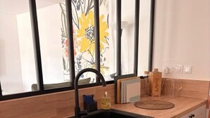 Una cocina con un lavamanos negro, encimera de madera y ventana con vistas a flores.