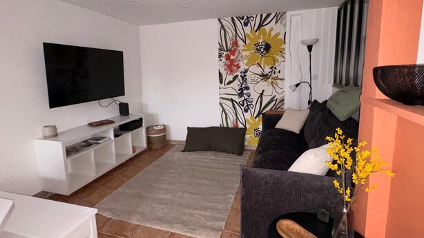 Una sala de estar con un televisor de pantalla plana, un sofá, una mesa de centro y una pared decorativa con motivos florales.