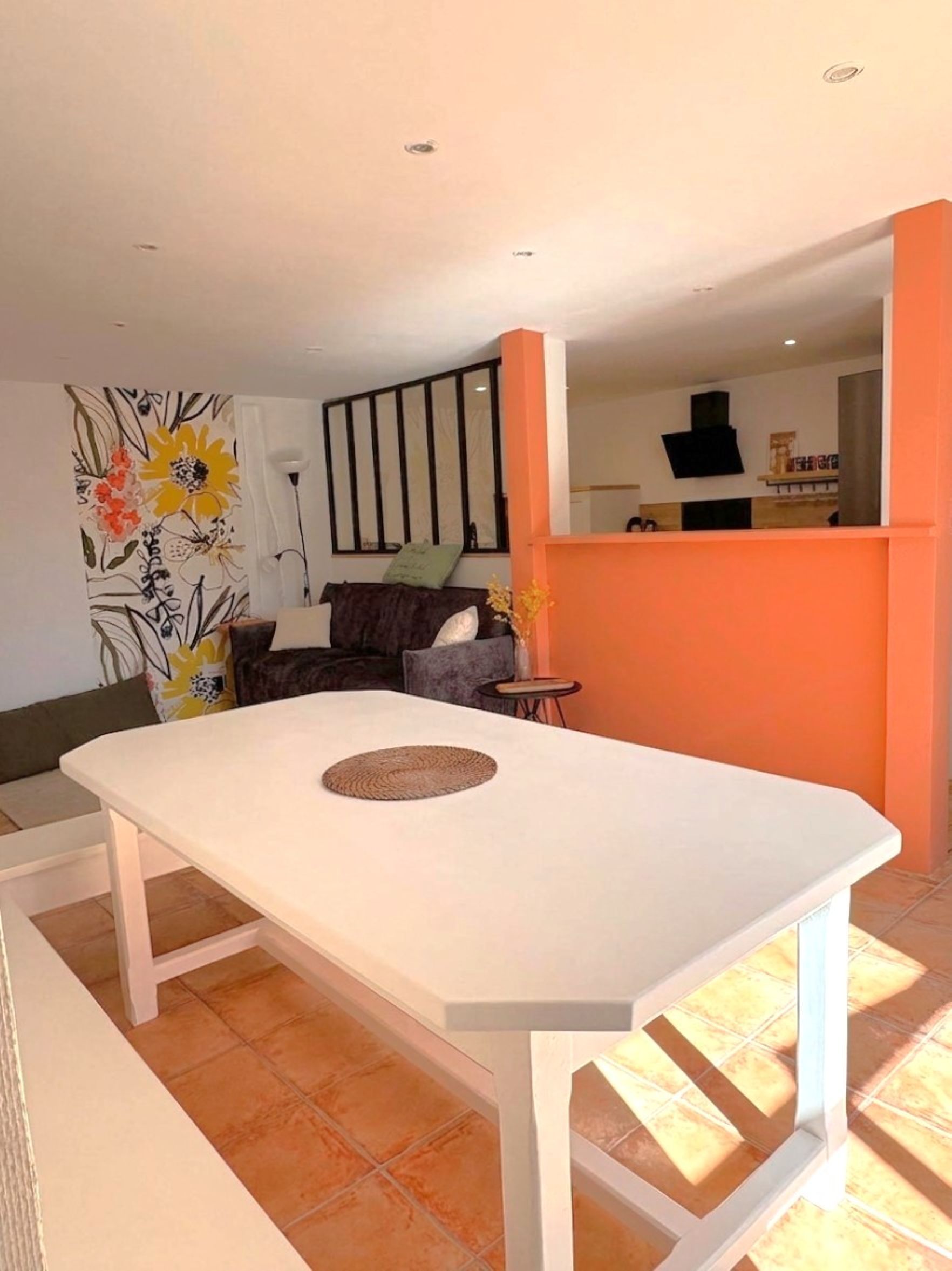 Een eetgedeelte met een witte tafel en stoelen, een decoratief vloerkleed en een bank op de achtergrond.