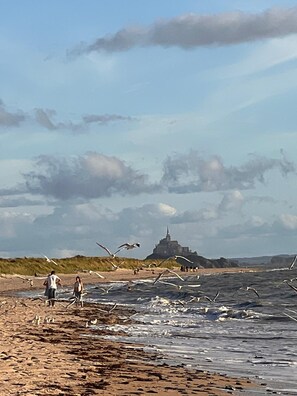 A beach with people and seagulls, a distant building, and a cloudy sky.