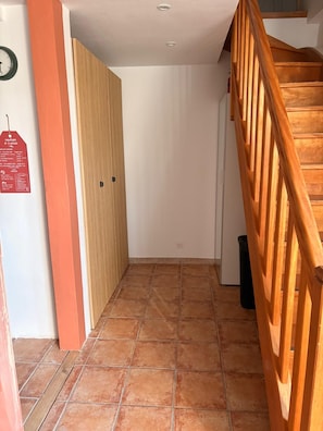 A hallway with a wooden staircase, a door, and a trash bin.