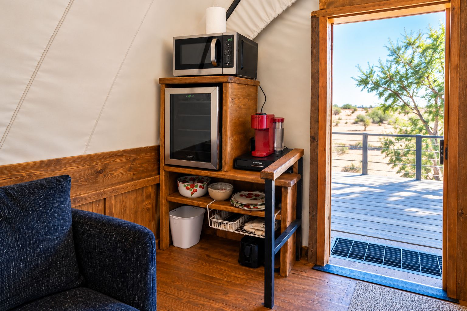 Un espacio habitable compacto con kitchenette, un estante de madera con electrodomésticos de cocina, vistas al exterior y una puerta que da a un área exterior.