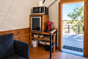 Een knus leefruimte met een kitchenette, een houten plank met keukenapparatuur, uitzicht op de omgeving en een deur naar een buitenruimte.