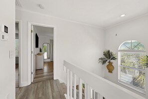 A hallway with a wooden floor, white walls, a white railing, and a window with blinds. - Heated Pool • Home Gym • Walk to Beach (Holmes Beach)
