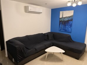 A room with a black sofa, a white coffee table, a blue accent wall, and an air conditioning unit.