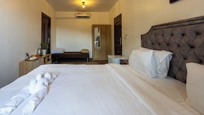 Quarto de hotel com uma cama grande, cabeceira de madeira, mesa de cabeceira, guarda-roupa e espelho.