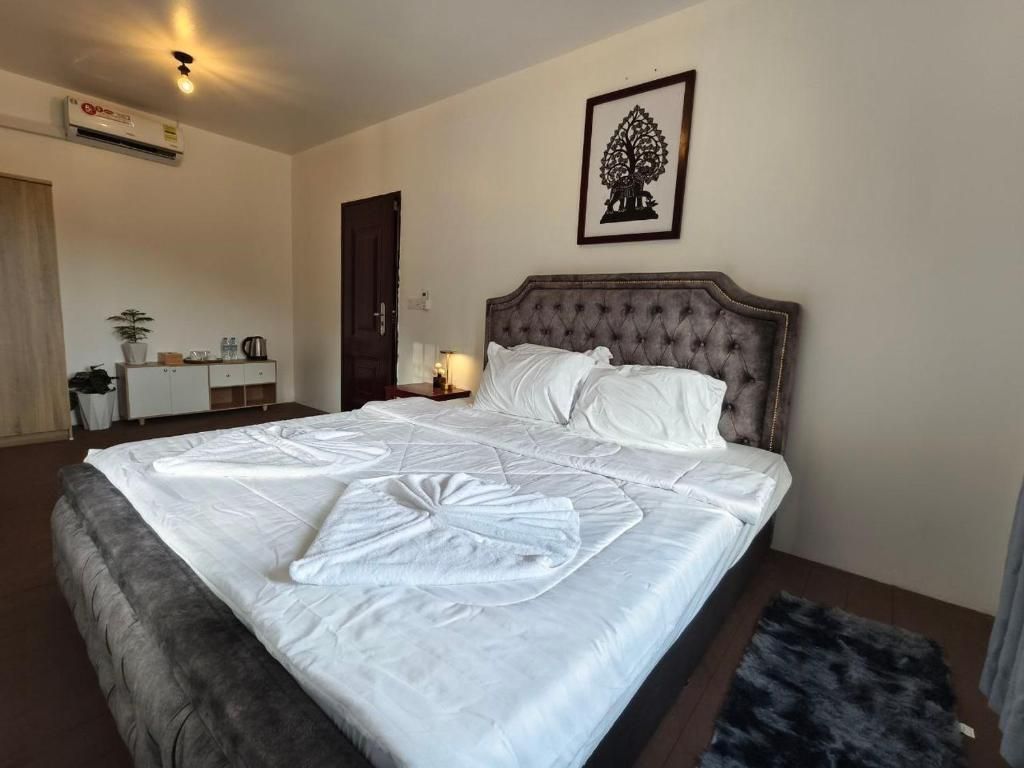 Una cama bien hecha con edredón y almohadas blancos, un cuadro en la pared y una mesita de noche con lámpara.