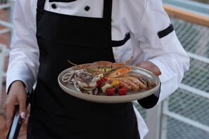 Una persona sostiene un plato con mariscos, incluyendo patas de cangrejo y calamares, junto con verduras.