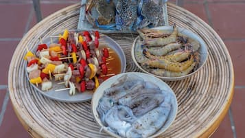 A round woven table with three dishes: skewers of meat and vegetables, a plate of shrimp, and a plate of fish.