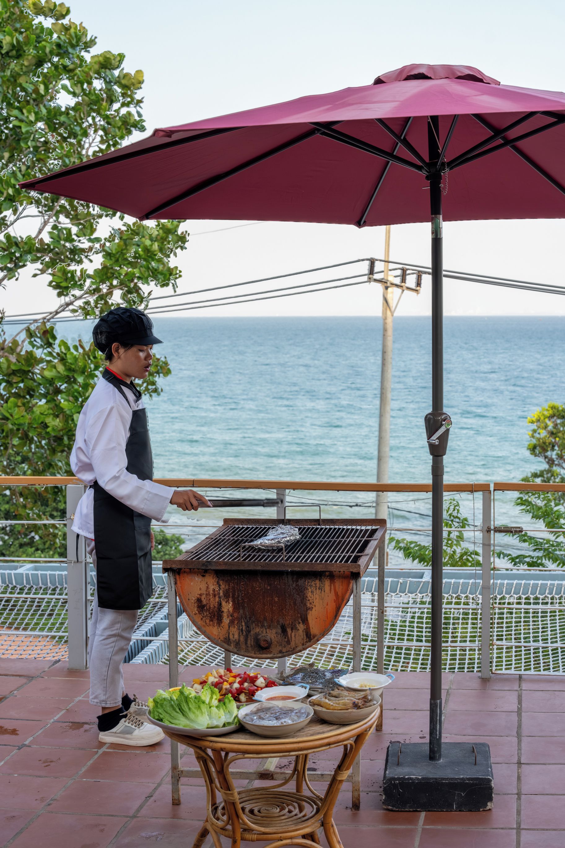 A person grilling outdoors with a view of the sea in the background.