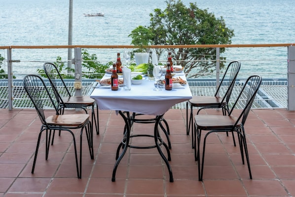 A table set for two with bottles and a glass on a terrace overlooking water.