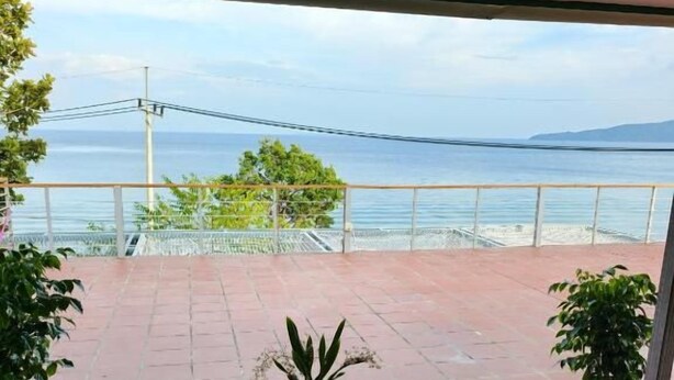 Varanda com mobiliário de vime e um vaso de planta, com vista para a praia e o mar.
