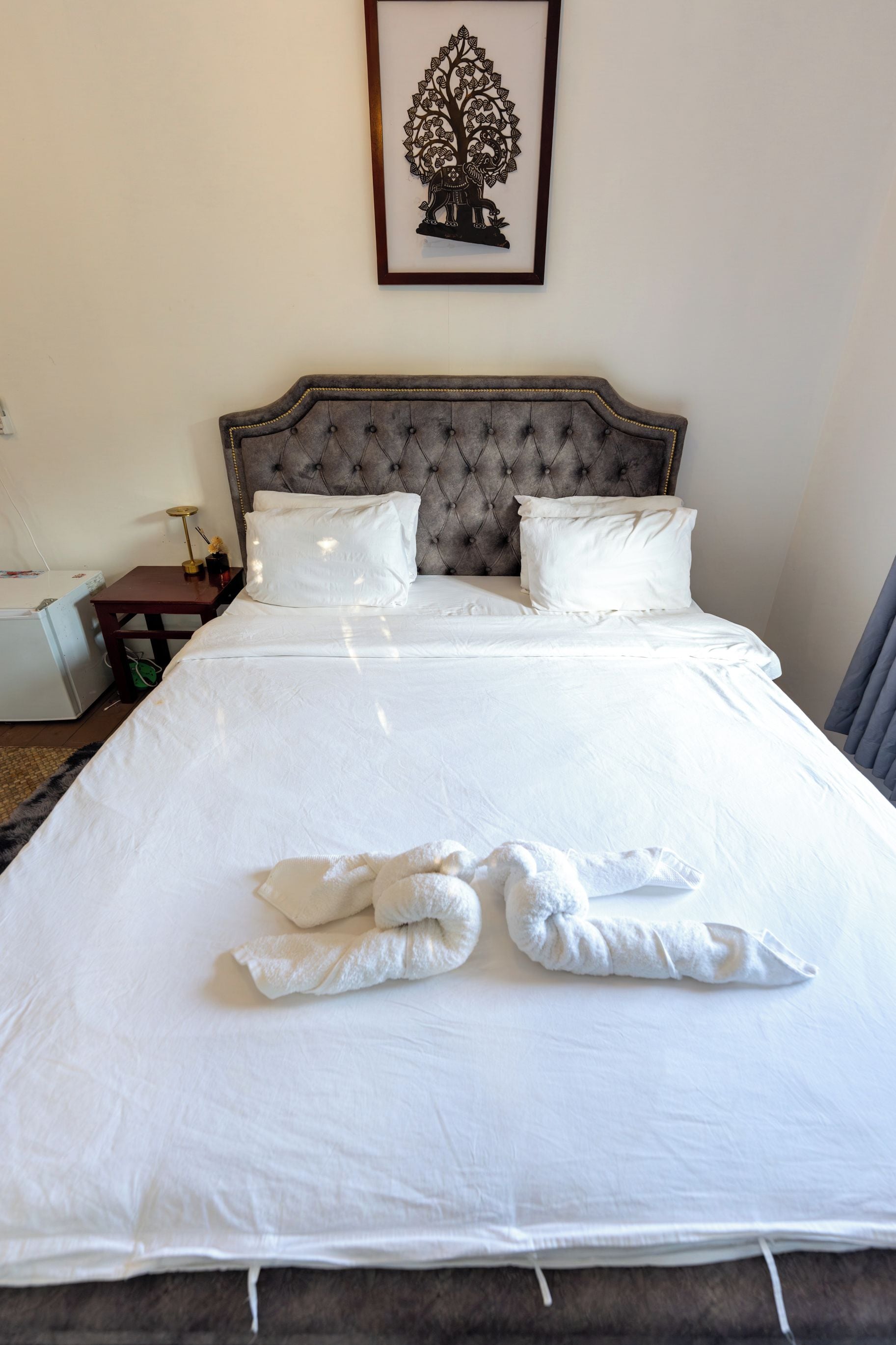A neatly made bed with white linens and two towels folded on the bed.