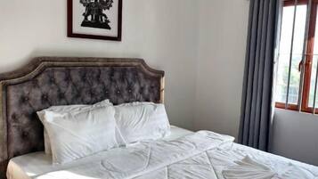 A neatly made bed with a headboard, a framed picture on the wall, and a window with curtains.