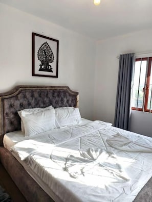 A neatly made bed with a headboard, a framed picture on the wall, and a window with curtains.