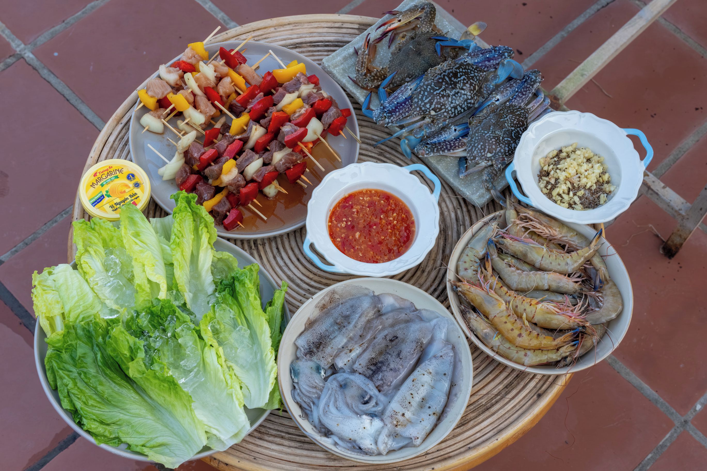 A variety of seafood including shrimp, crab, and fish, along with skewers of meat and vegetables, and a bowl of sauce.