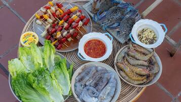 A variety of seafood including shrimp, crab, and fish, along with skewers of meat and vegetables, and a bowl of sauce.