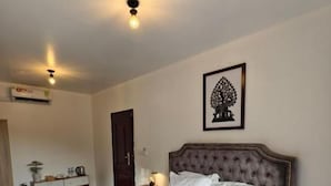 Cama bem arrumada com colcha branca decorativa, cabeceira e quadro na parede.
