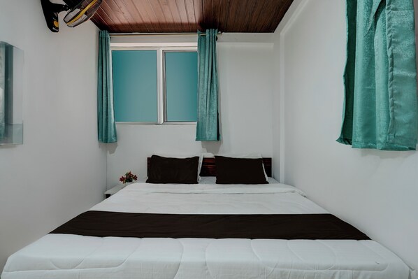A single bed with white bedding, two dark pillows, teal curtains, and a wooden ceiling.