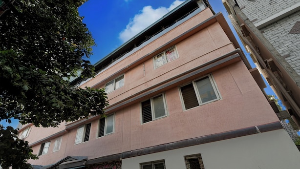 A multi-story building with a pink facade, multiple windows, and a visible tree in the foreground. - Hotel O Kodgehalli Railway Station (Bangalore)