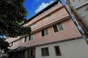 A multi-story building with a pink facade, multiple windows, and a visible tree in the foreground.
