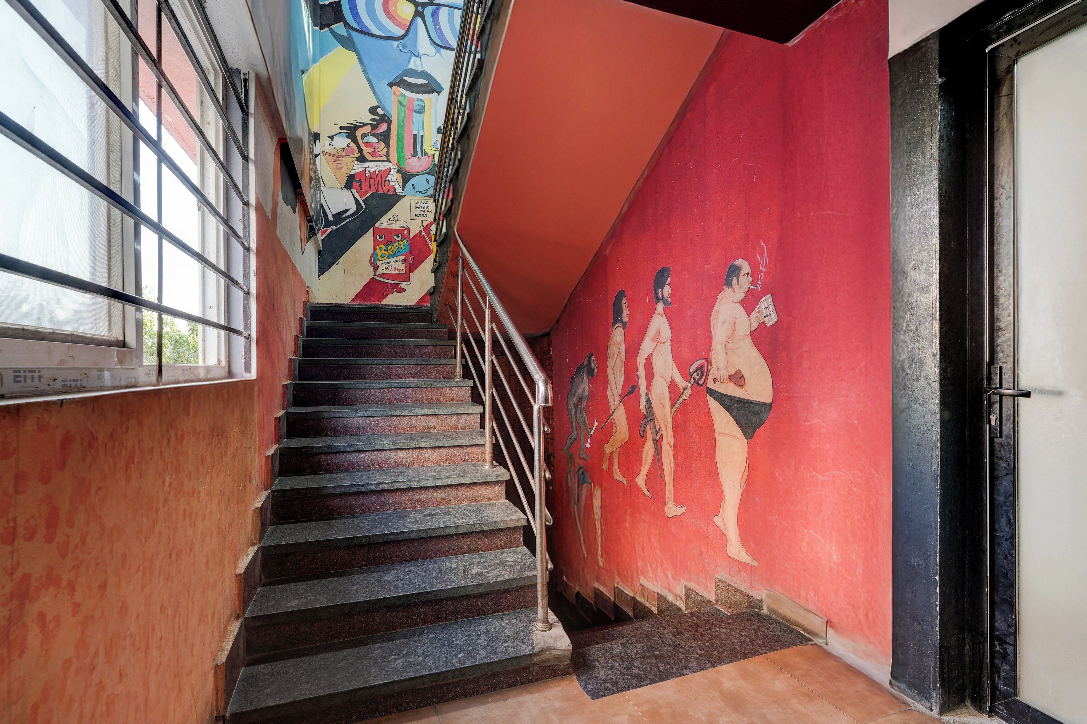 Una escalera con un mural en la pared, barandales metálicos y una puerta a la derecha.