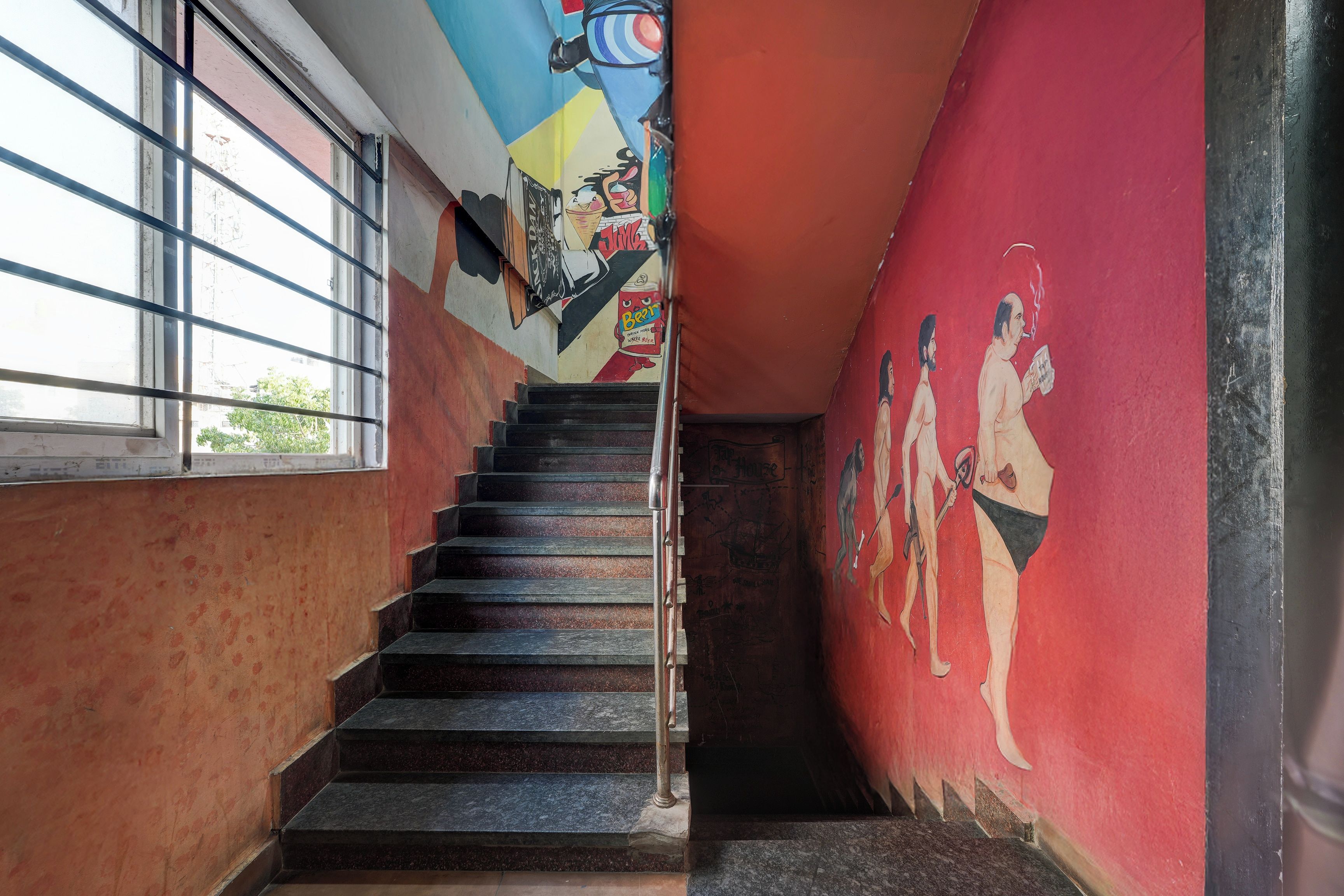 Una escalera con barandilla que lleva a una habitación con pared roja y un mural.