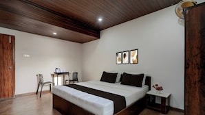 A bedroom with a large bed, a desk, chairs, and a small table with a vase of flowers. - Hotel O Kodgehalli Railway Station (Bangalore)