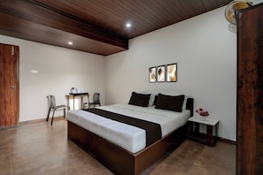Ein Schlafzimmer mit einem großen Bett, einem Schreibtisch, Stühlen und einem kleinen Tisch mit einer Blumenvase.
