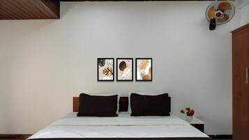 Un dormitorio con cama, dos almohadas, una mesita de noche, un florero con flores y tres cuadros en la pared.