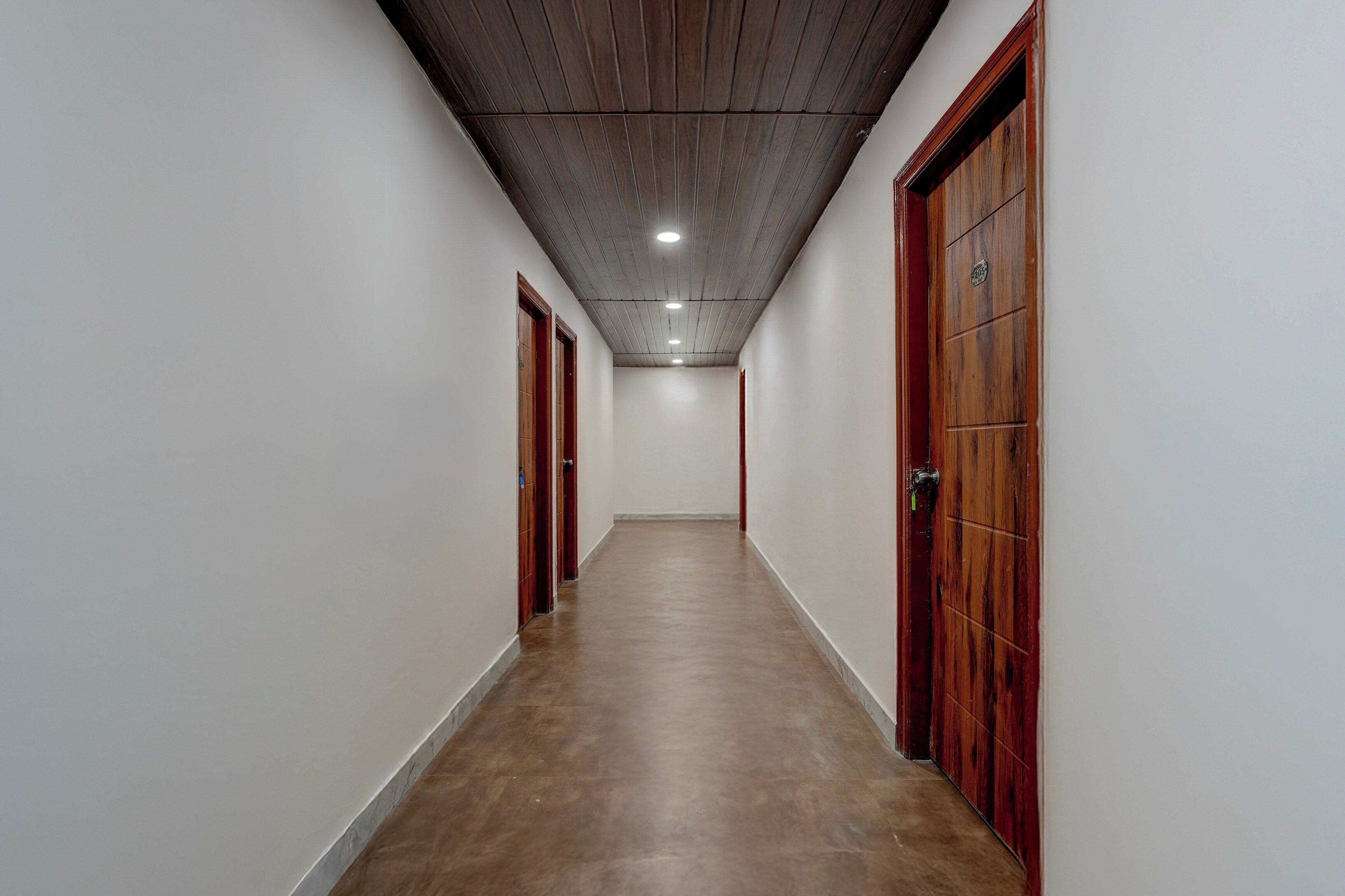 Un pasillo con puertas de madera y suelo de baldosas, que conduce a una habitación con techo de madera e iluminación empotrada.