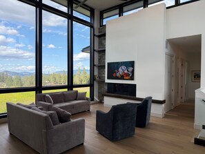 A modern living room with a fireplace, a large window with a view of the outdoors, and a painting on the wall. - New luxury 4 bedroom/4 bathroom home on vineyard with pool and panoramic views. (Kelowna)