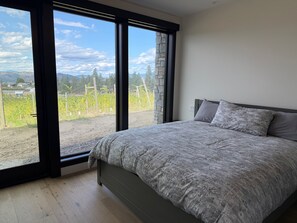 Ein Schlafzimmer mit einem großen Bett, Blick auf einen Weinberg und einer Steinmauer.