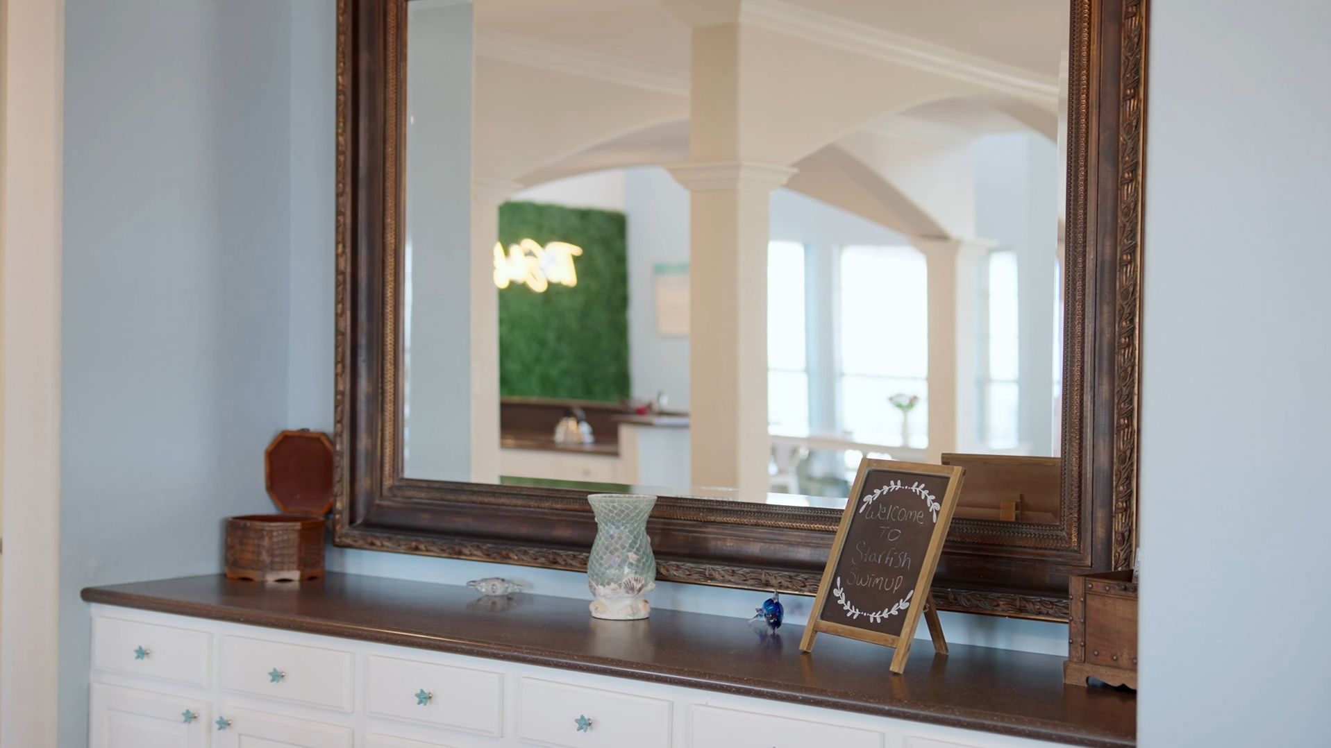 A mirror with a wooden frame, a small chalkboard sign, and decorative items on a dresser.