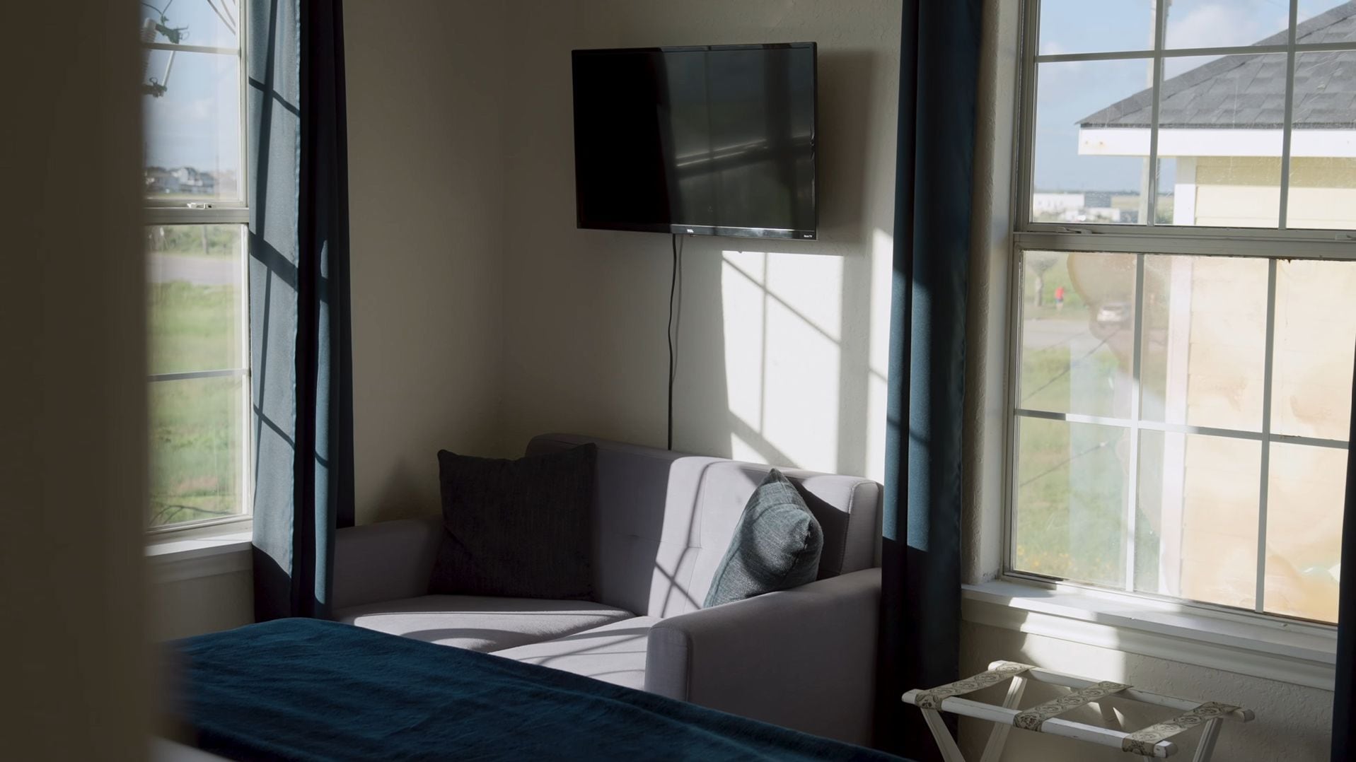A room with a bed, a chair, a television mounted on the wall, and a window with a view of the outside.