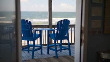 A wooden deck with two blue chairs and a table, overlooking the ocean.