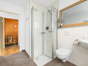 A modern bathroom with a glass-enclosed shower, a white toilet, and a sink with a mirror above. - NEW - Schleikubus (Kappeln)