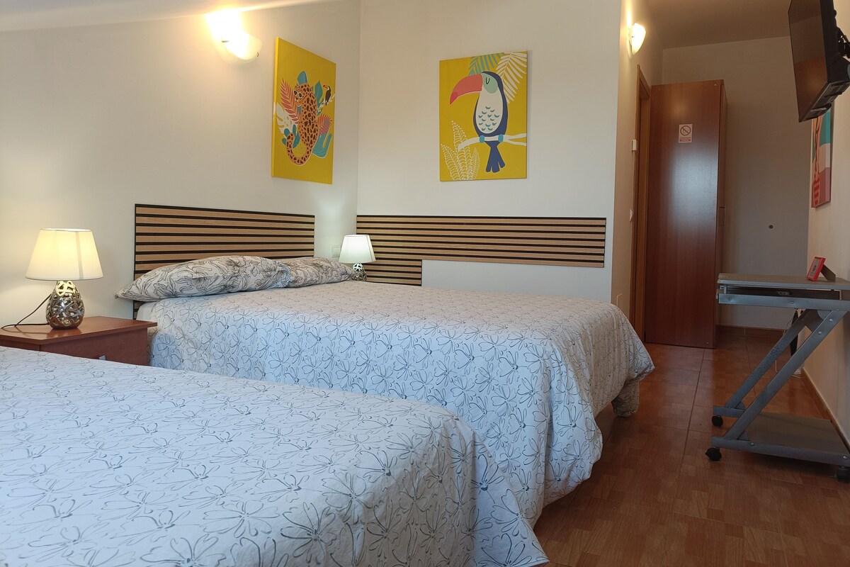A hotel room with two beds, a desk, and artwork on the walls.