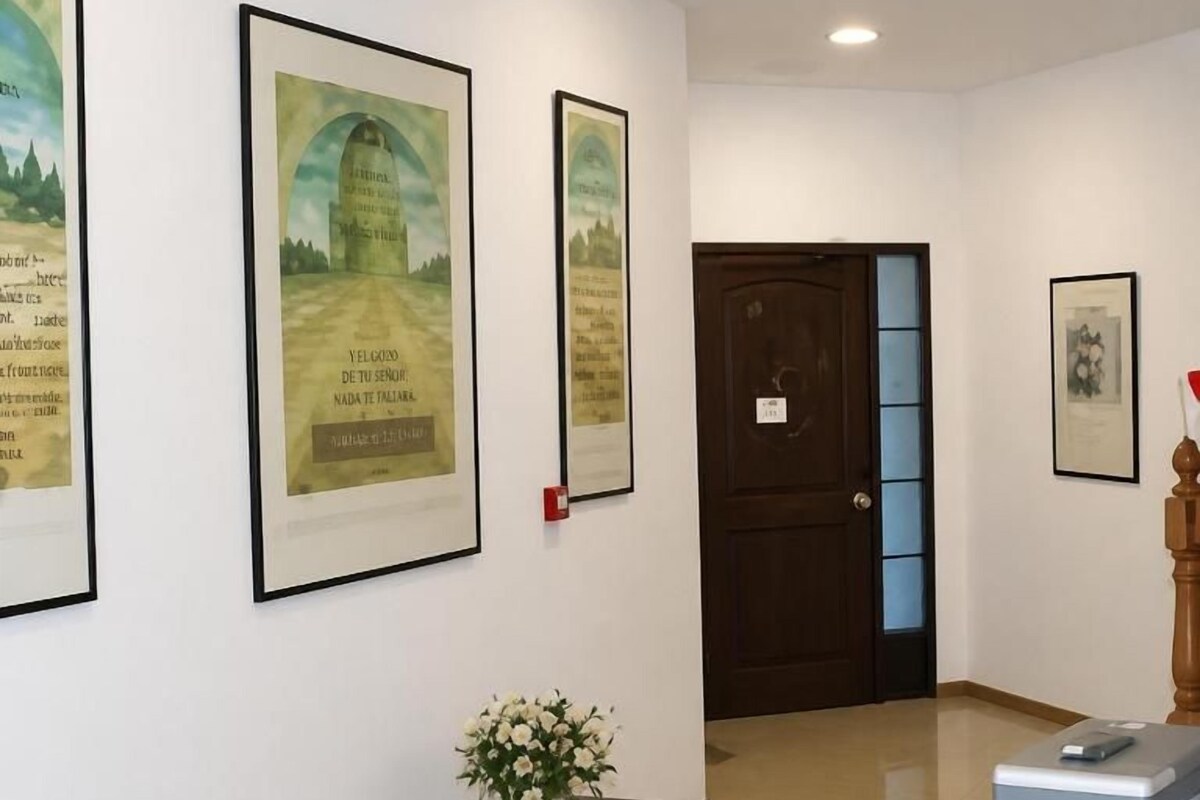 A hallway with framed artwork on the walls, a wooden door, a small table with a vase of flowers, and a reception desk.