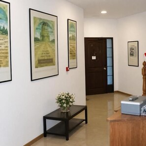 A hallway with framed artwork on the walls, a wooden door, a small table with a vase of flowers, and a reception desk. - Hostal Las Eras- Cubillos del Sil (Cubillos del Sil)