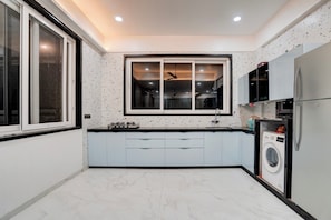 A compact kitchen with a gas stove, a washing machine, and a refrigerator. - DanCenter Villa Viva 5BHK with Pvt Pool (Lonavala)