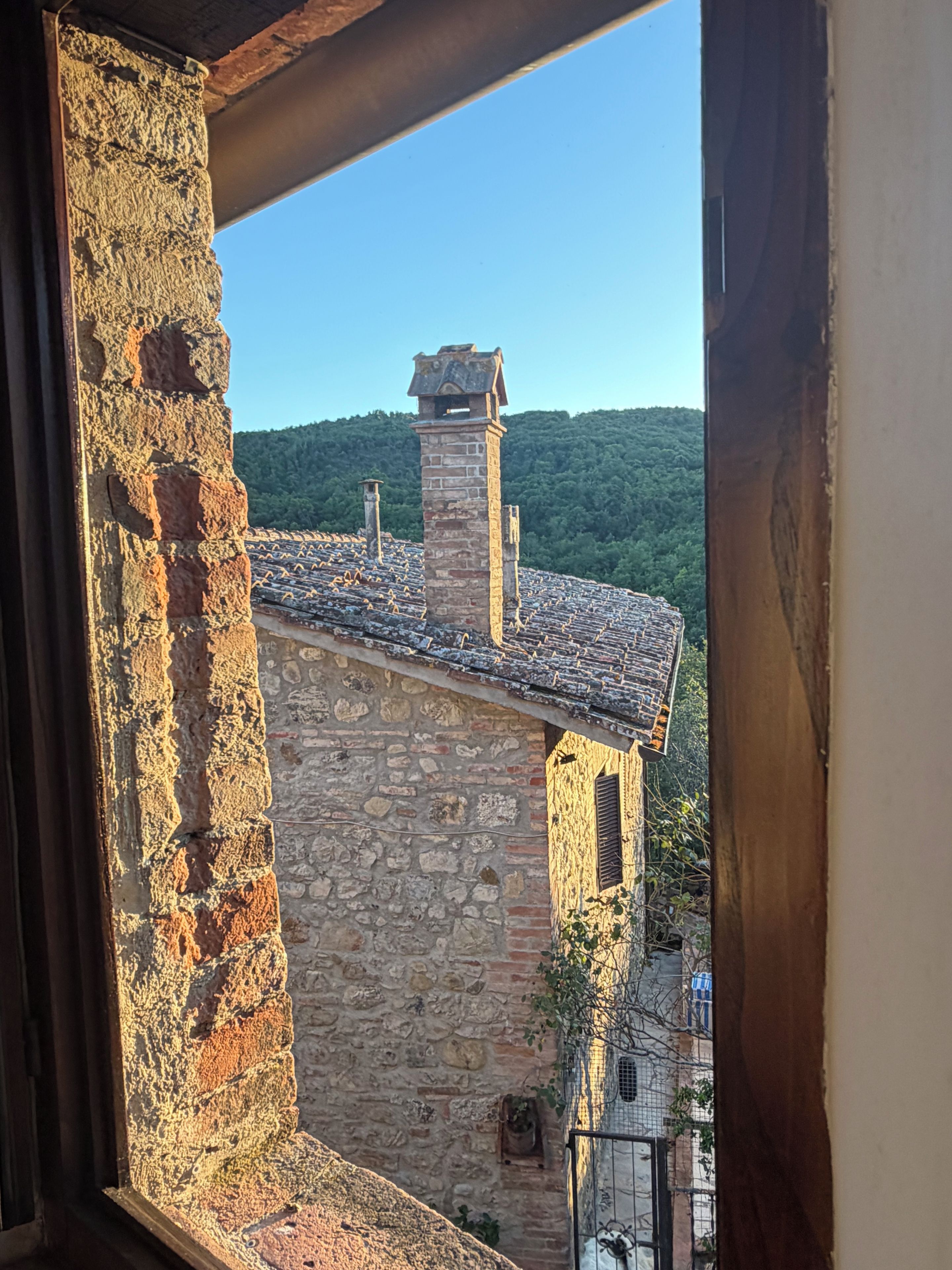 Ein Gebäude aus Stein mit einem Ziegeldach und einem Schornstein, gesehen durch ein Fenster mit Holzrahmen.